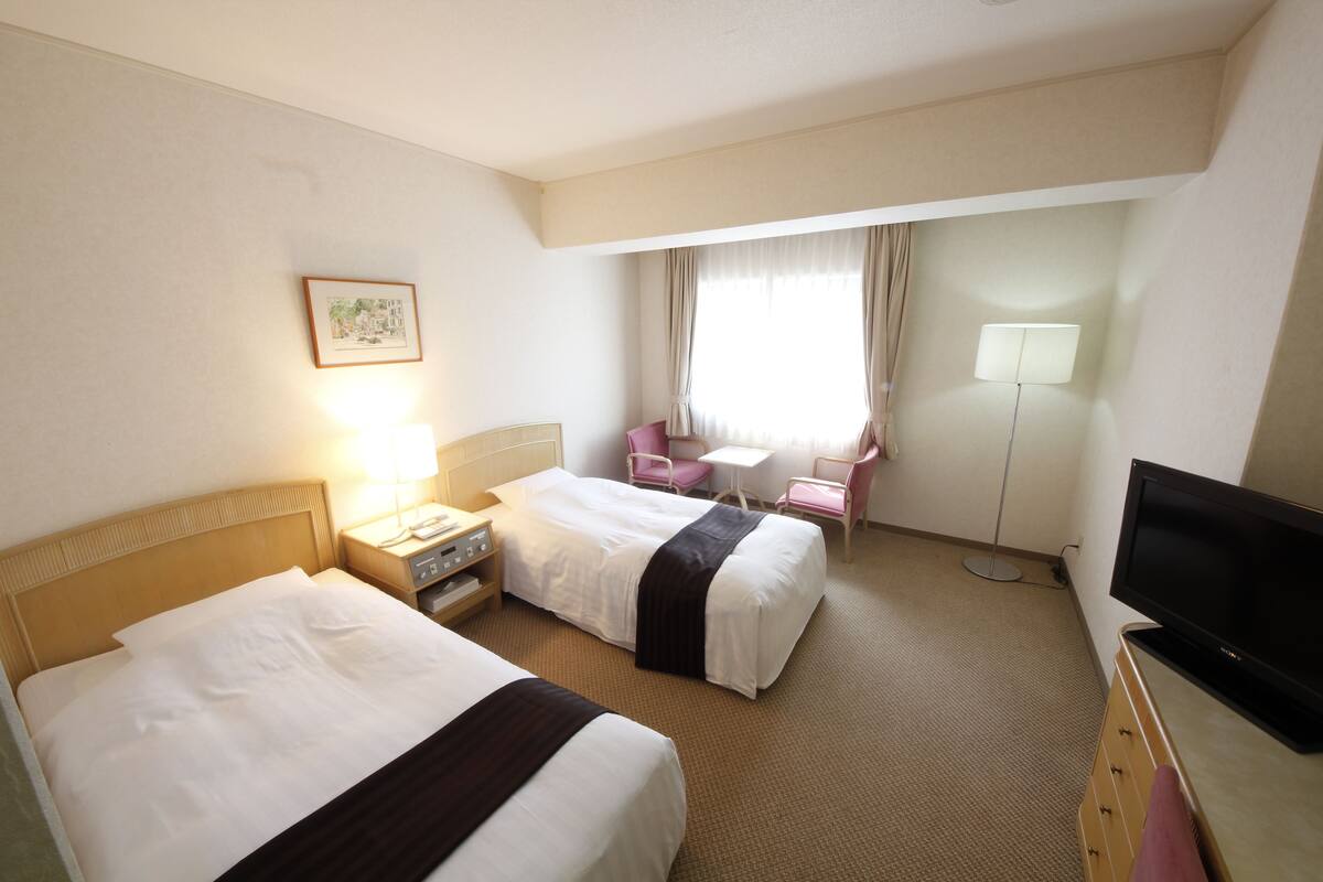 Hotelkamer met twee bedden, een bureau, een stoel, een televisie en een raam met gordijnen.