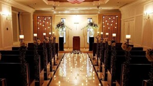 Eine Hotellobby mit einem langen, glänzenden Marmorboden, Reihen schwarzer Stühle und zwei üppigen Blumenarrangements am Ende.
