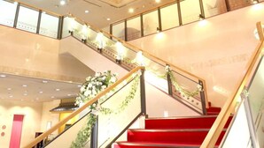 Ein mehrgeschossiges Interieur mit einer zentralen Treppe, Glasgeländern und einem dekorativen Chandelier.