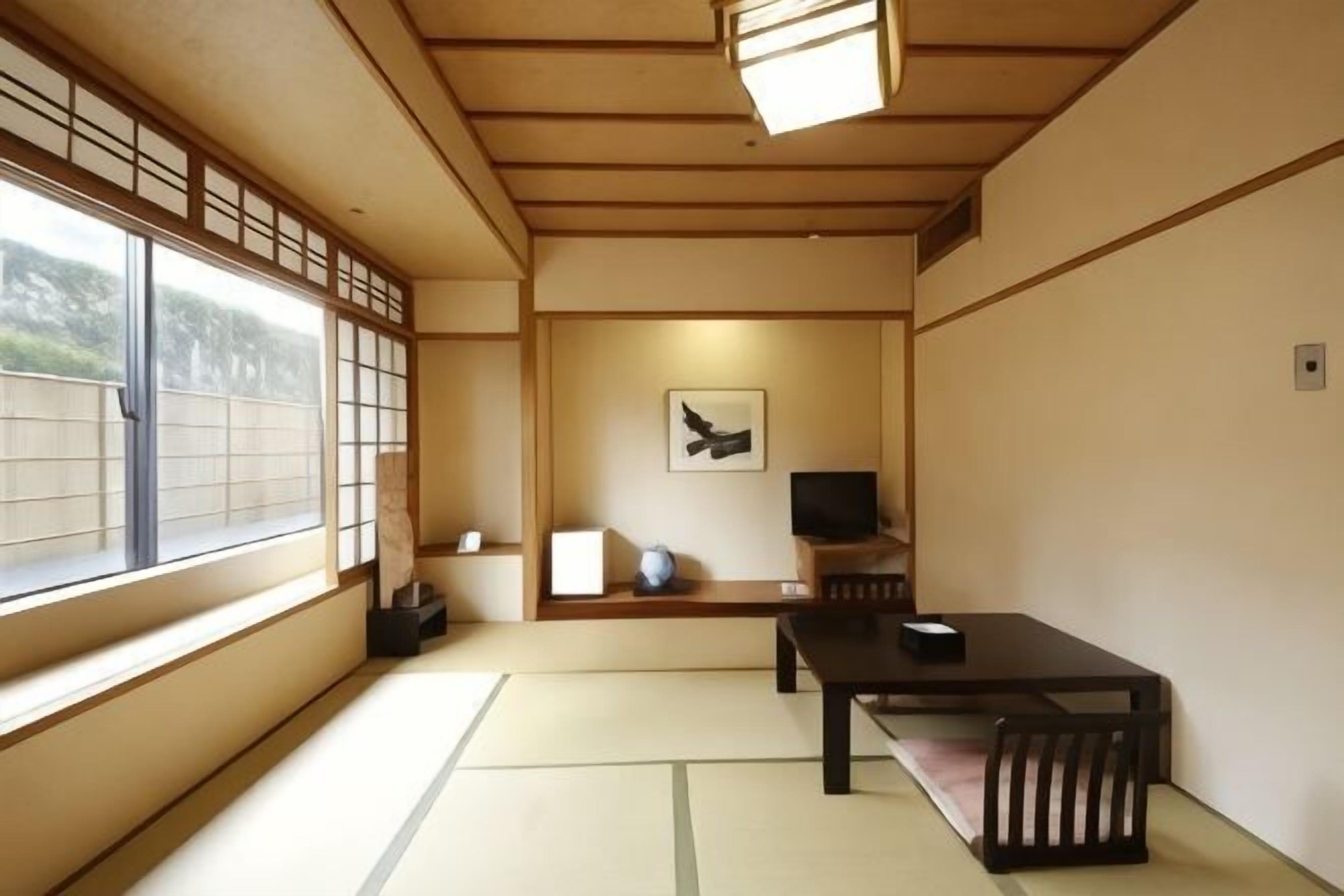 A traditional Japanese room with tatami flooring, a low table with a bench, a television, and a framed artwork on the wall.