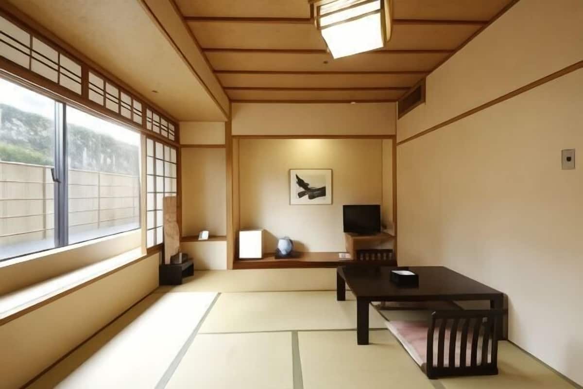 A traditional Japanese room with tatami flooring, a low table with a bench, a television, and a framed artwork on the wall.