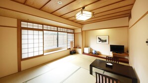 Ein traditioneller japanischer Raum mit Tatami-Boden, einem niedrigen Tisch mit Stühlen, einem Fernseher und einem Shoji-Bildschirm.