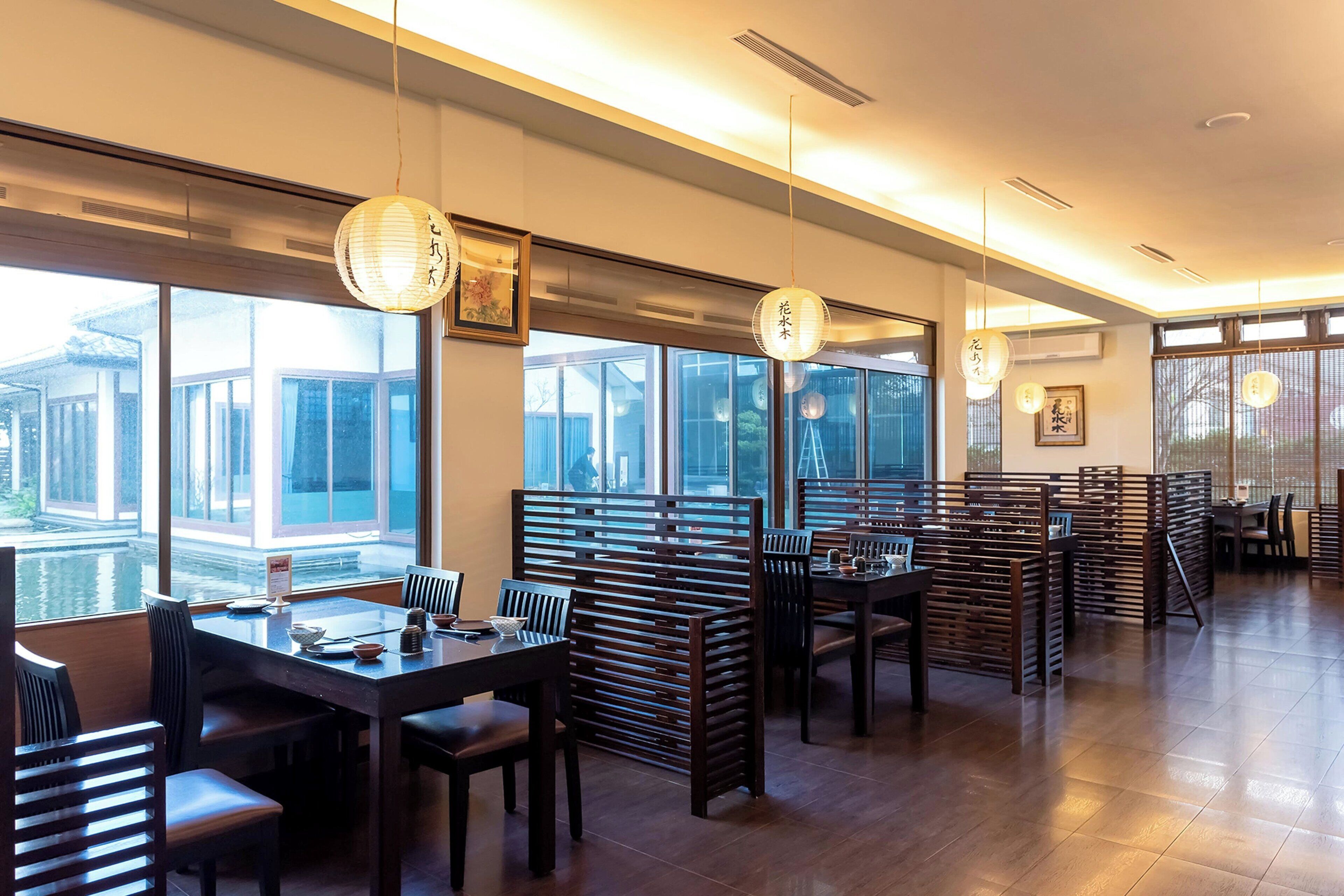 A restaurant with wooden furniture, large windows, and hanging paper lanterns.