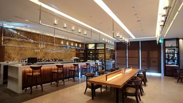 A modern bar area with a long wooden table, bar stools, and a wine rack with bottles.