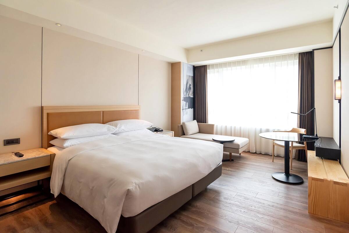 Ein modernes Hotelzimmer mit einem großen Bett, einem Schreibtisch, einem Sessel und einem kleinen Tisch.