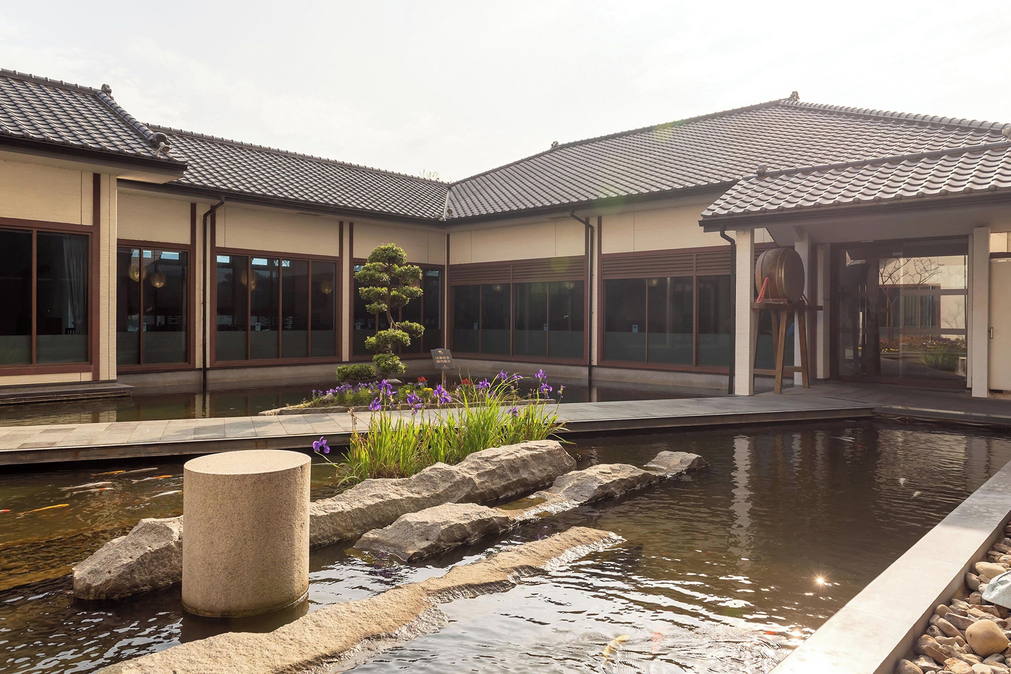 A traditional building with a tiled roof, a koi pond, and a stone lantern.