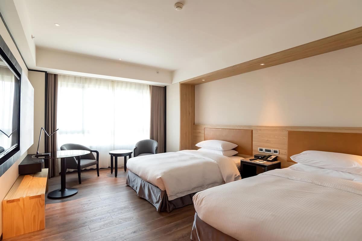 Ein Hotelzimmer mit zwei Betten, einem Schreibtisch, einem Stuhl und einem kleinen Tisch.