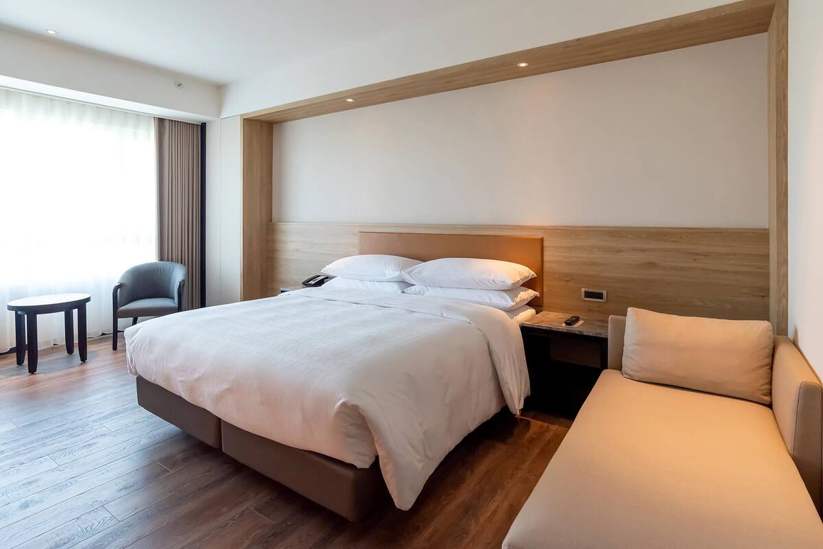 Ein modernes Hotelzimmer mit einem großen Bett, einem Nachttisch, einem Sessel und einem kleinen Tisch.