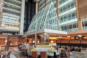 A modern hotel lobby with a glass atrium, seating areas, and a central decorative tree. - Sheraton Taoyuan Hotel (Taoyuan City)