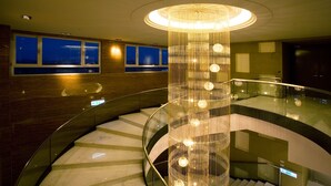 A multi-level interior with a central spiral staircase, a decorative chandelier, and a view of the city at night through large windows.