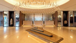A modern lobby with a central reception desk, a large chandelier, and a polished marble floor.