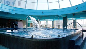 An indoor swimming pool with a glass ceiling, water jets, and lounge chairs.