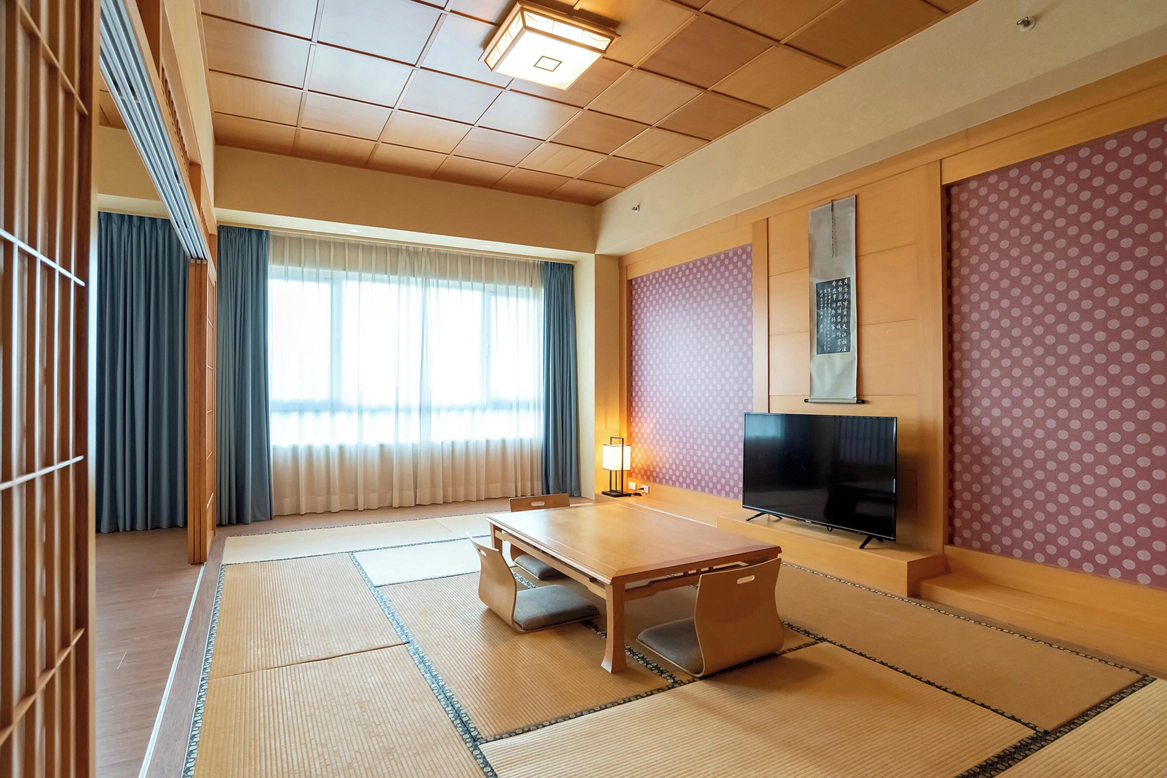 Une pièce de style japonais traditionnel, avec un sol recouvert de tatamis, une petite table en bois, un téléviseur et des portes coulissantes.