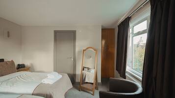 Habitación de hotel con dos camas, una silla de madera, un espejo y un ventanal con cortinas.