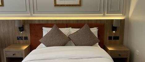 A neatly made bed with two pillows, a framed picture above, and two bedside lamps.