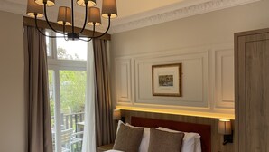 Habitación de hotel con una cama grande, una araña de cristal, un cuadro en la pared y vistas al exterior.