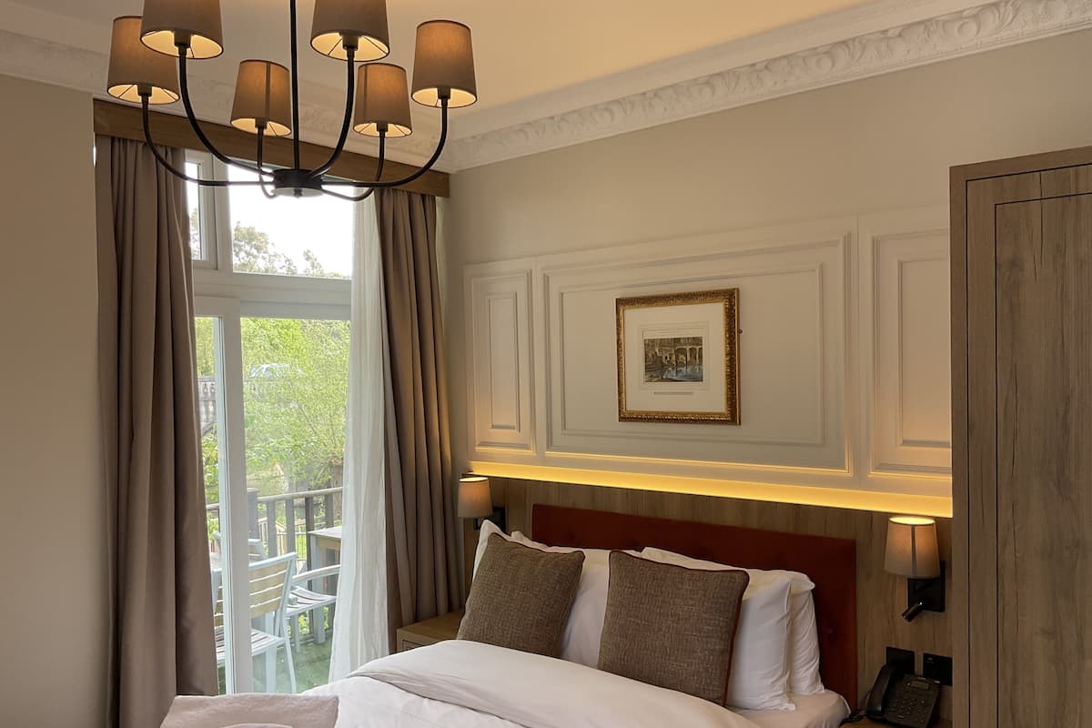 A hotel room with a large bed, a chandelier, a picture on the wall, and a view of the outdoors.