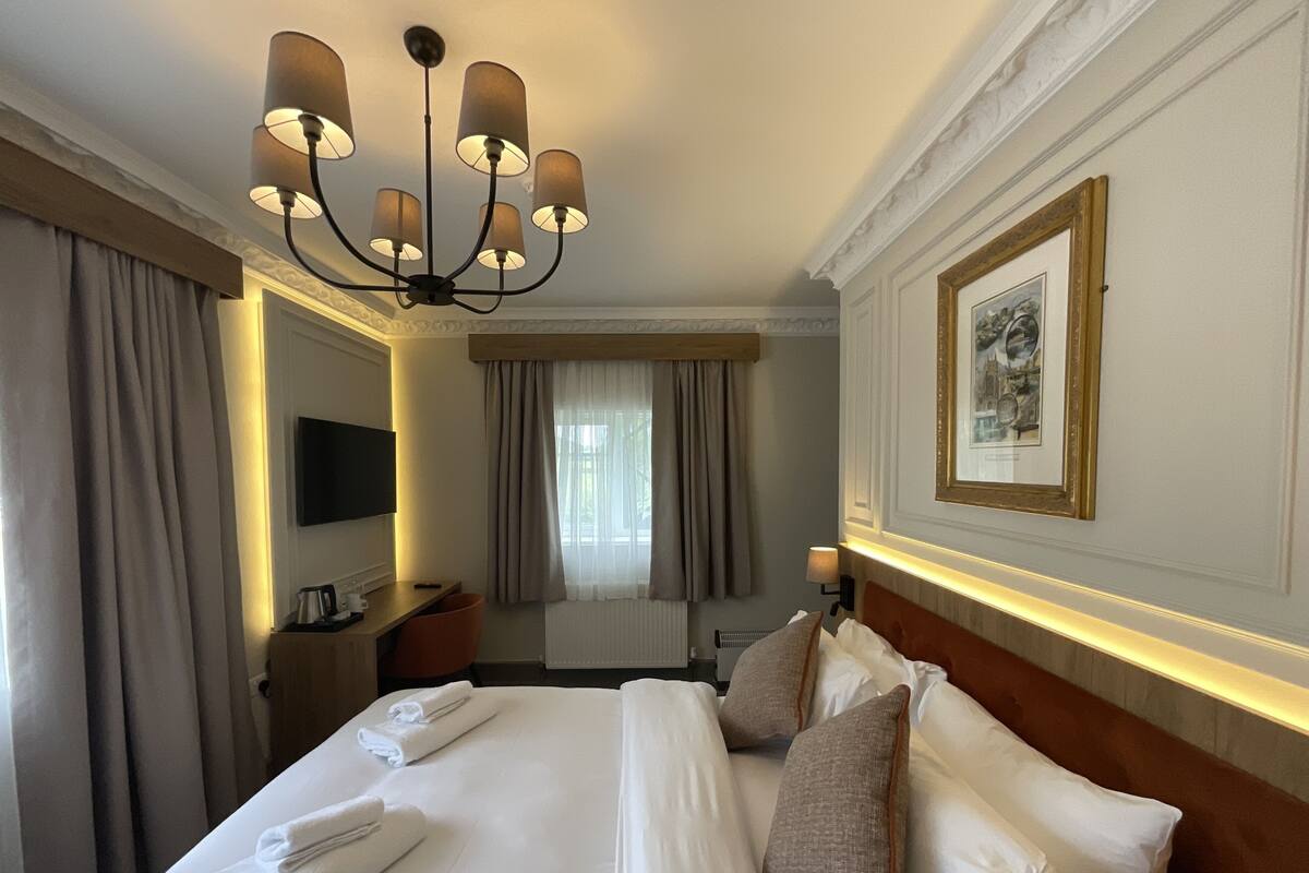 A hotel room with a large bed, a television, a desk, and a window with curtains.