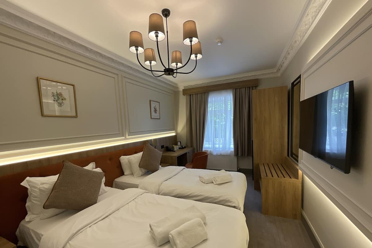 A hotel room with two beds, a TV, a desk, and a window with curtains.