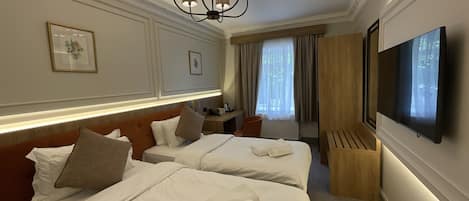 A hotel room with two beds, a TV, a desk, and a window with curtains.