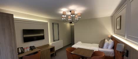 Ett hotellrum med en säng, ett skrivbord, en stol, en tv och en kristallkrona.