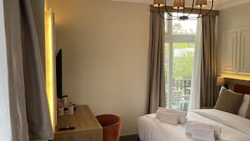 A hotel room with a bed, a desk, a chair, a TV, and a balcony with curtains.