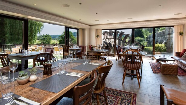 Un comedor amplio con varias mesas y sillas, ventanas grandes que ofrecen vistas panorámicas y una combinación de asientos interiores y exteriores.
