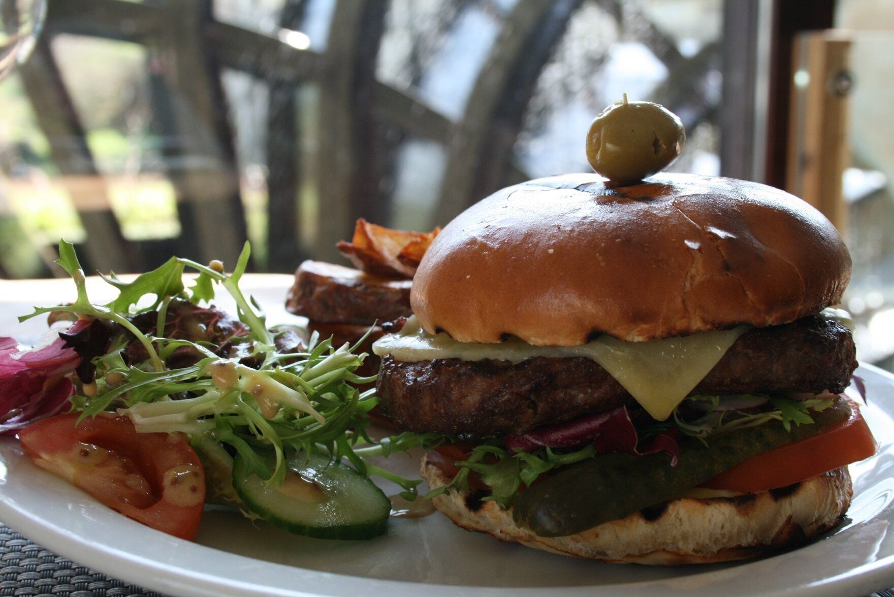 A burger with a bun, cheese, lettuce, tomato, and a pickle on a plate.