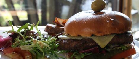 A burger with a bun, cheese, lettuce, tomato, and a pickle on a plate.