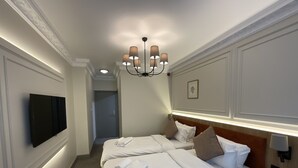 Habitación de hotel con dos camas, un televisor montado en la pared, una araña y un cuadro enmarcado.