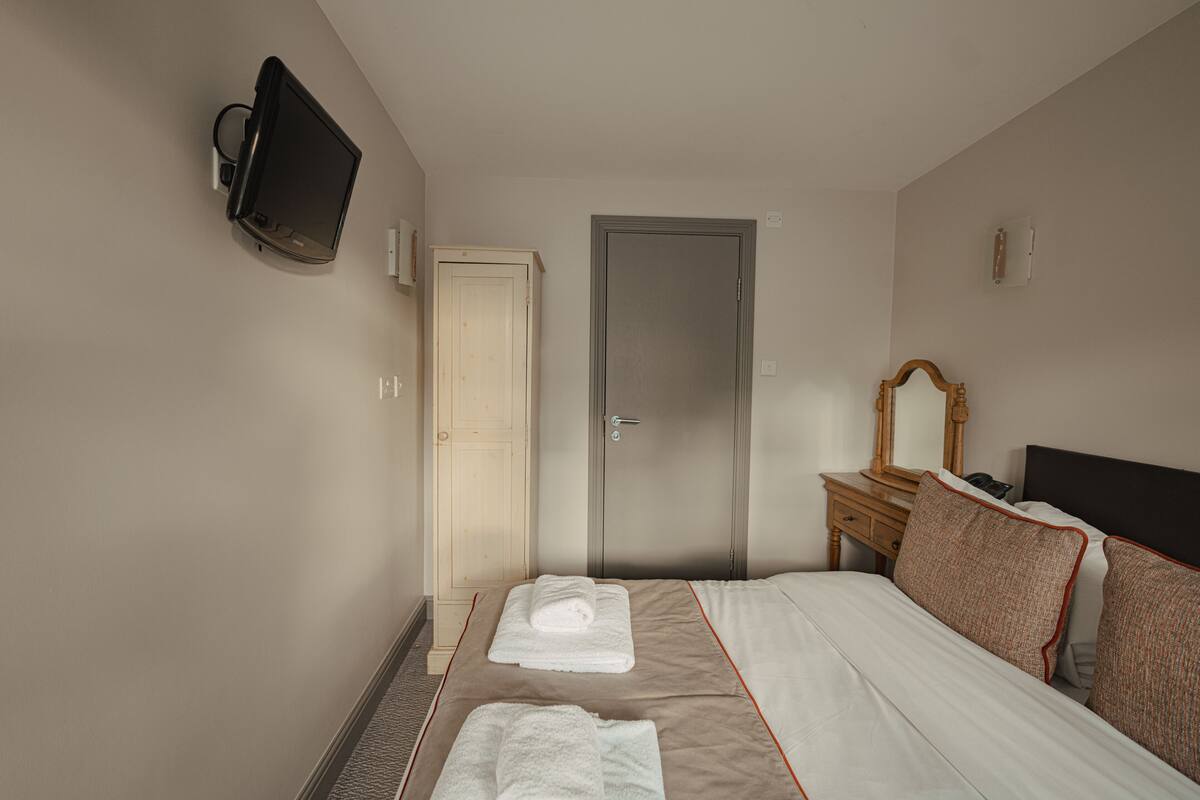A hotel room with a bed, a television mounted on the wall, a door, and a bedside table with a mirror.