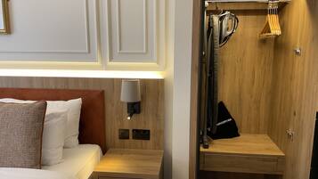 A hotel room with a bed, bedside table, lamp, and a wooden closet with hanging clothes.