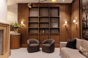 Un interior moderno con una estantería de madera, dos sillones, un sofá y un escritorio con un jarrón de flores.