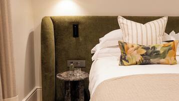 A hotel room with a bed, a bedside table, a lamp, and a small round table with a bottle and glass.