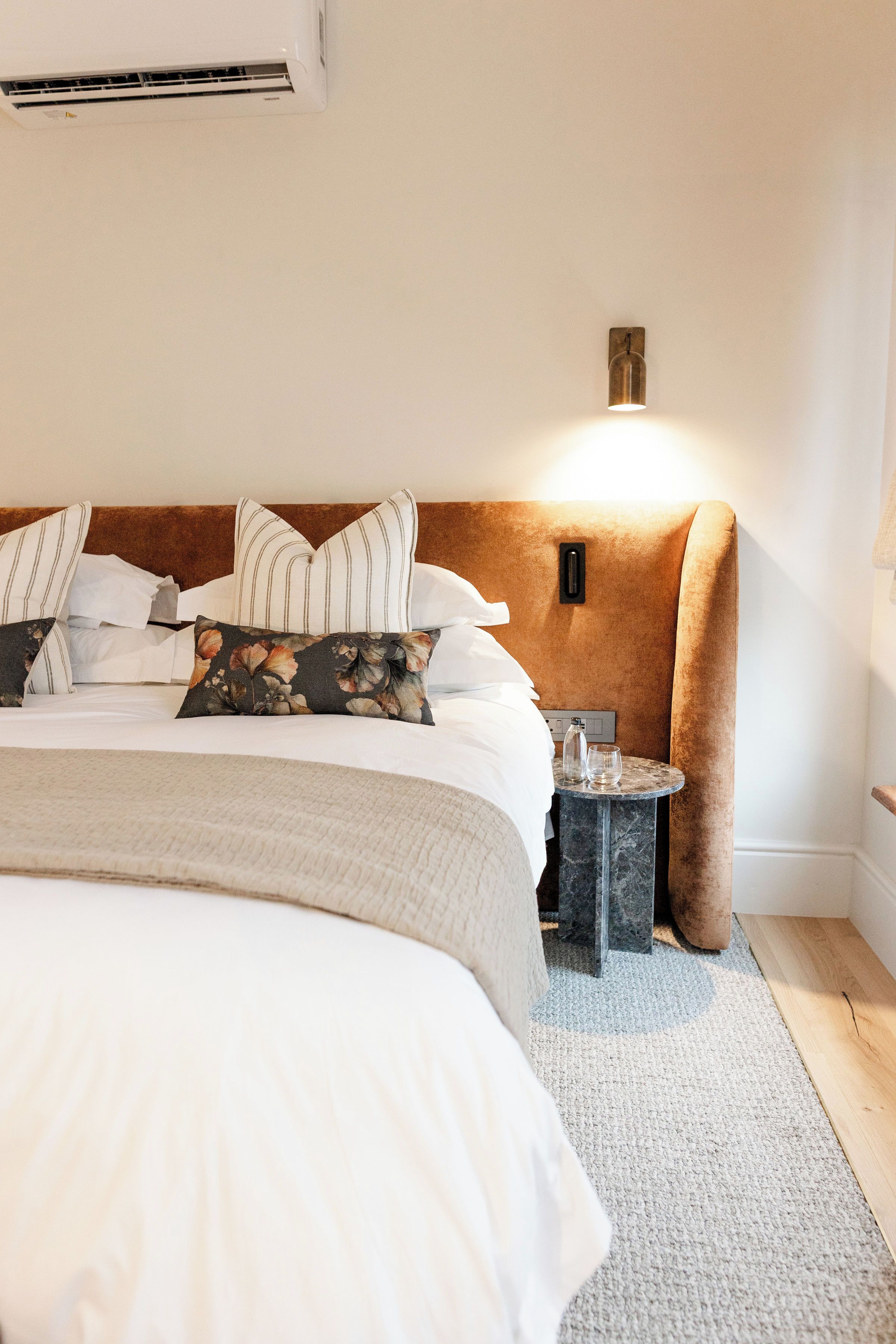 Una habitación de hotel con una cama, almohadas, una mesita de noche y una lámpara fijada a la pared.