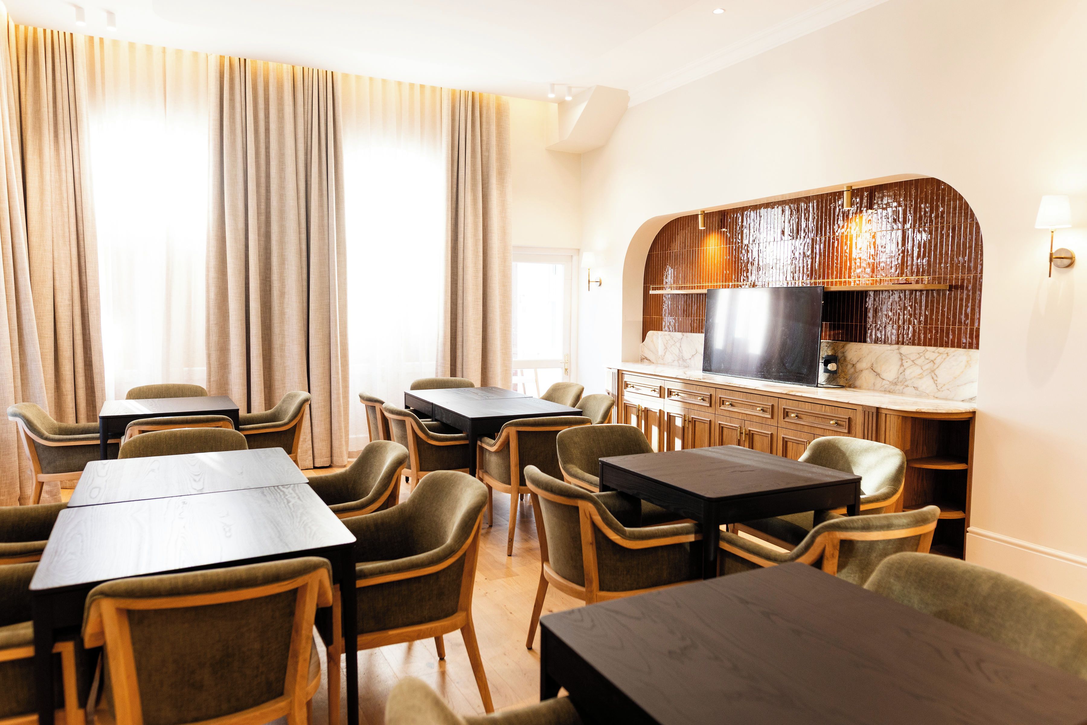A hotel room with a dining area, a kitchen with a marble countertop, and a large window with curtains.