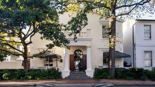 A historic building with a grand entrance, a covered outdoor seating area, and a well-maintained garden. - Eendracht Hotel (Stellenbosch)