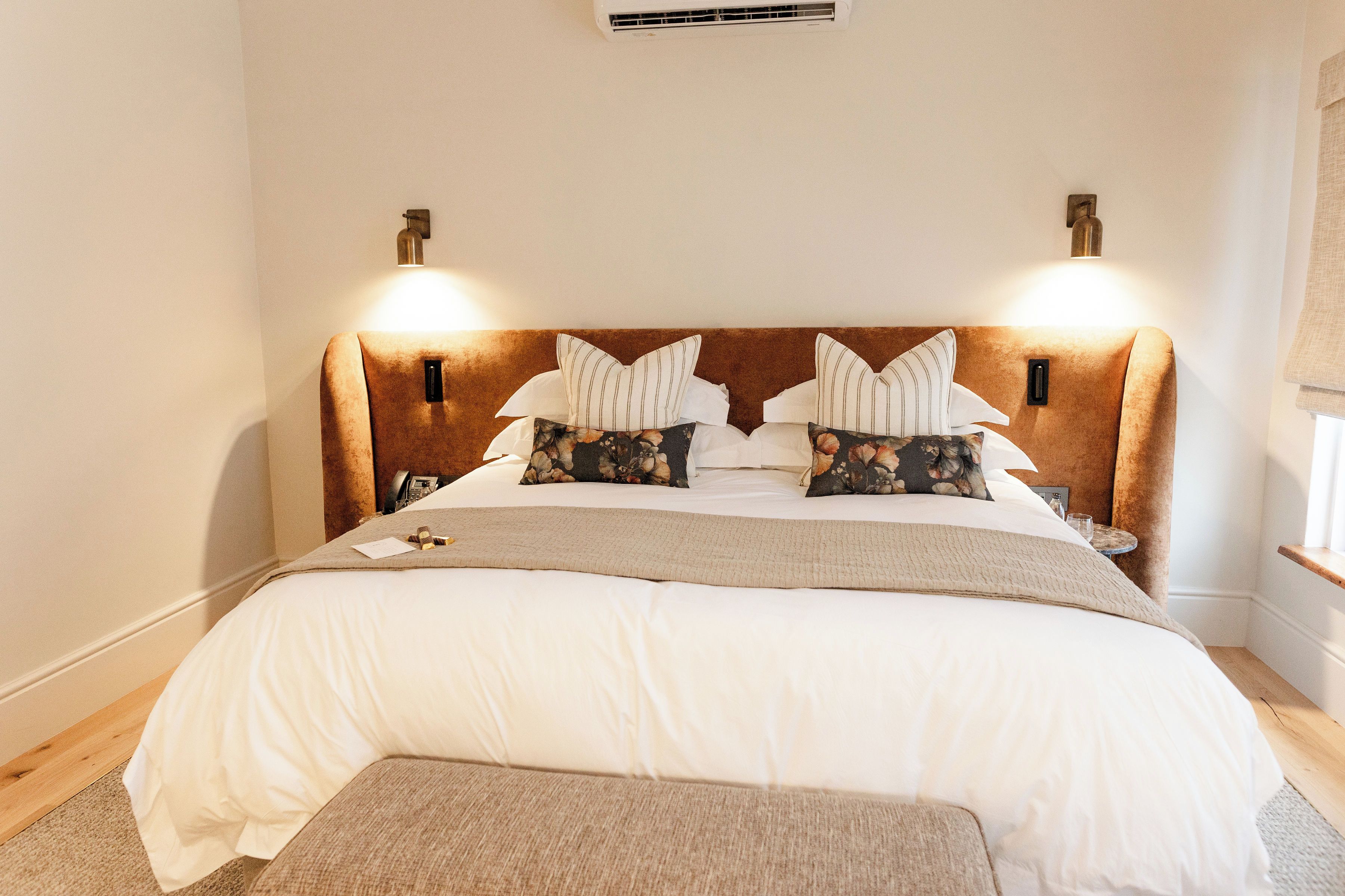 A neatly made bed with a headboard, two bedside lamps, and a bedside table with a glass.