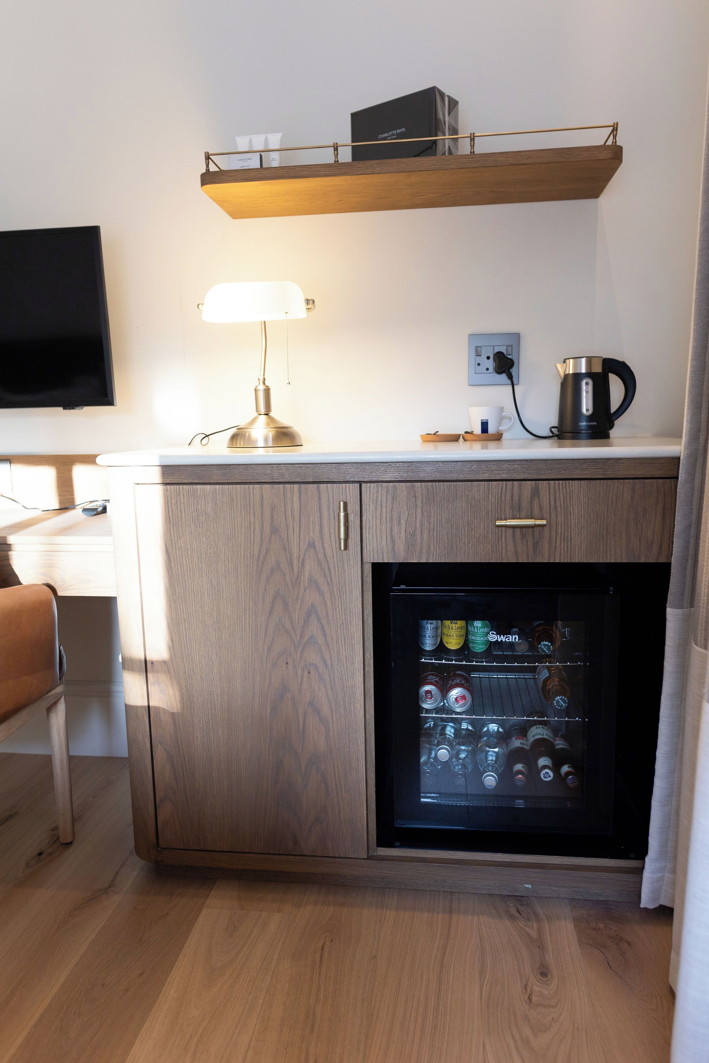 A compact kitchenette with a built-in refrigerator, a coffee maker, and a flat-screen TV mounted on the wall.