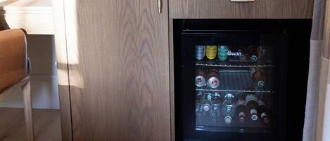 A compact kitchenette with a built-in refrigerator, a coffee maker, and a flat-screen TV mounted on the wall.