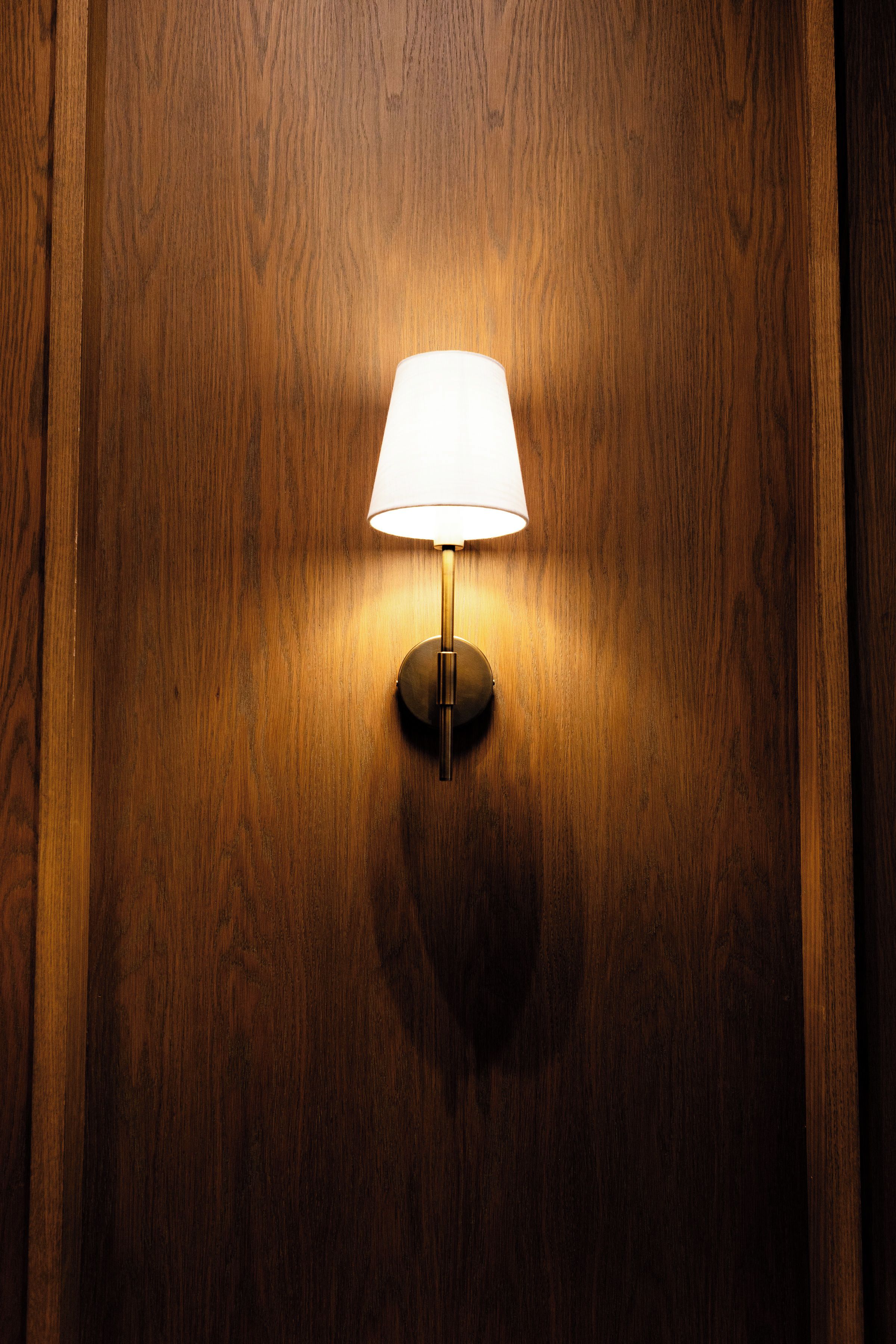 Une lampe de sol fixée au mur, dotée d’un abat-jour blanc, placée devant un mur en bois.