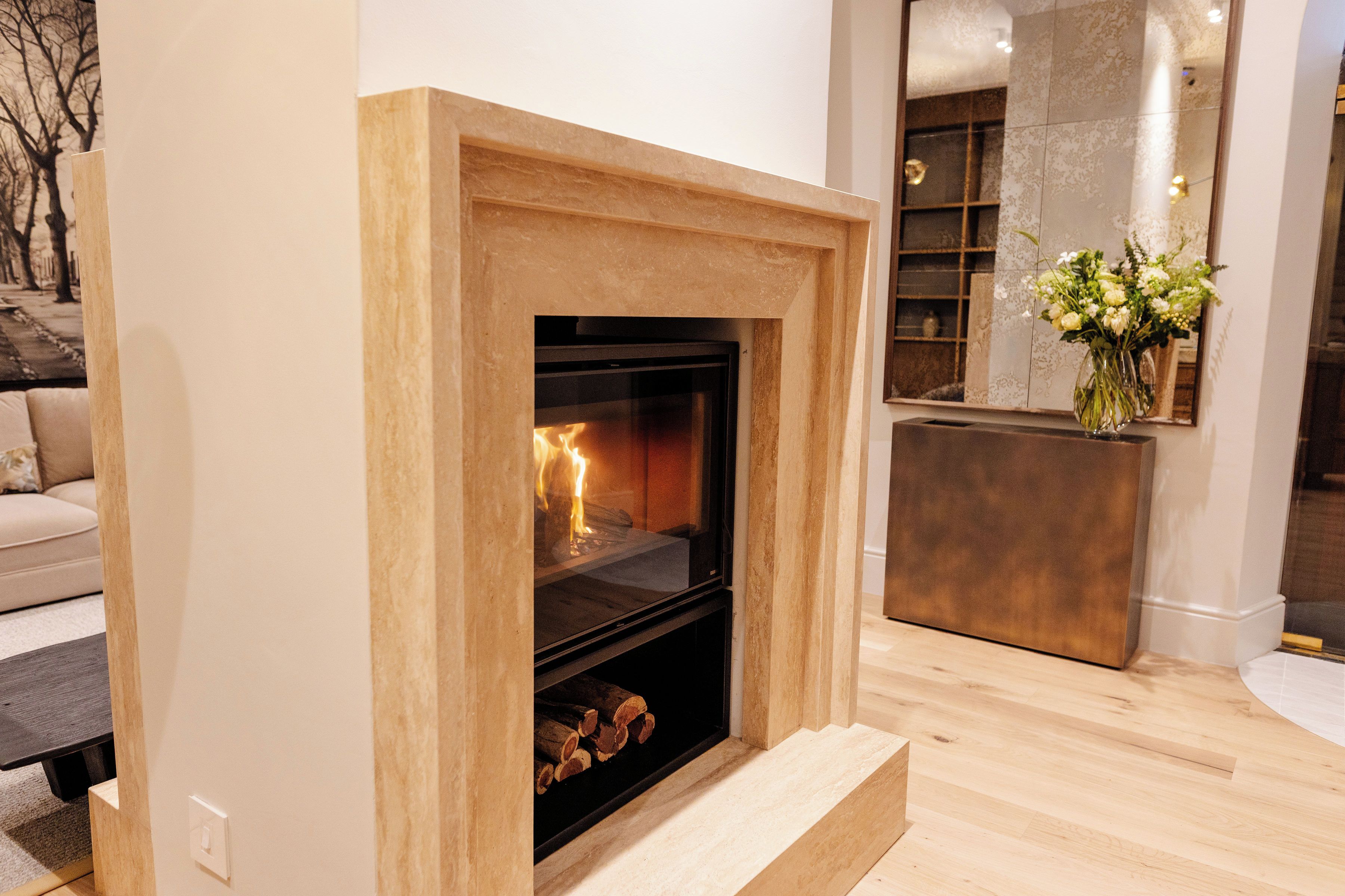 Una chimenea con repisa de madera, un espejo encima y un florero con flores a la derecha.
