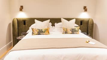 Una cama bien tendida con una colcha color beige y dos almohadas florales, flanqueada por dos lámparas de pared.