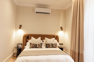 Una habitación de hotel con cama, mesitas de noche, aire acondicionado y una cortina.