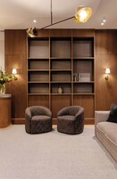 Una sala moderna con dos sillones redondos, un sofá, una estantería empotrada de madera y una lámpara colgante.