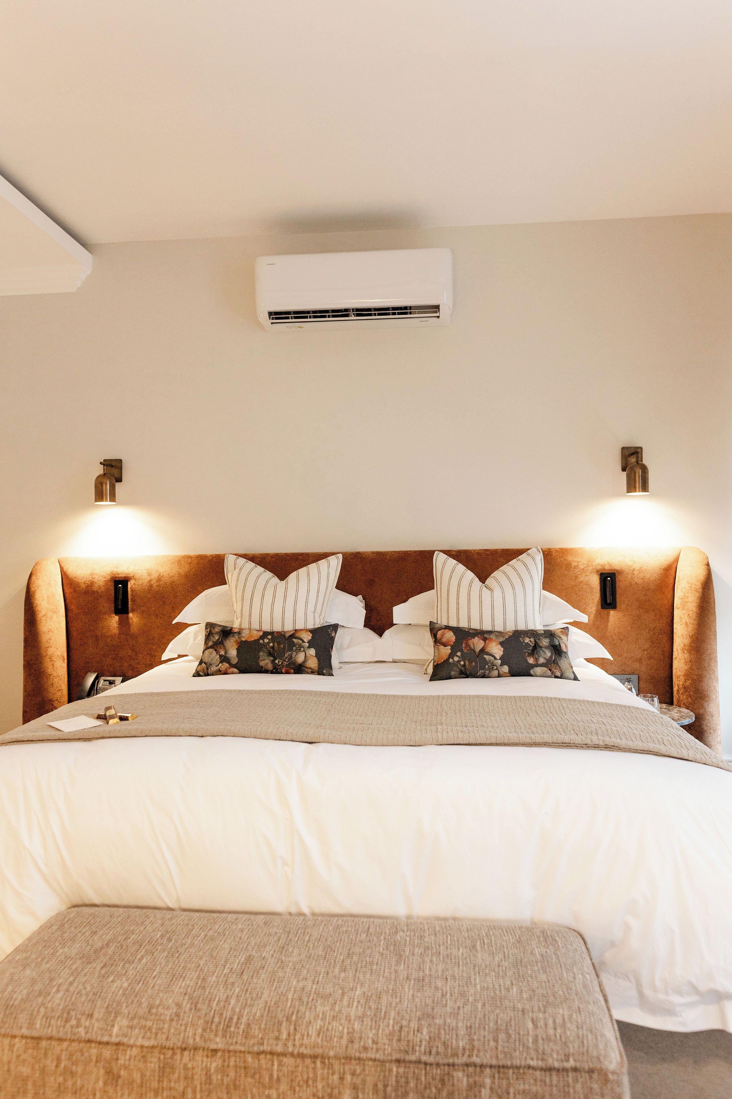 Ein Hotelzimmer mit einem großen Bett, zwei Nachttischlampen, einer Wand-Klimaanlage und einem kleinen Nachttisch.