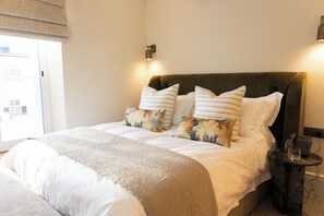 A hotel room with a bed, pillows, a bedside table with a phone, and a window with blinds. - Eendracht Hotel (Stellenbosch)