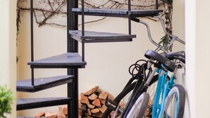 A spiral staircase with a metal railing, a blue bicycle leaning against the wall, and a stack of firewood at the base. - Eendracht Hotel (Stellenbosch)