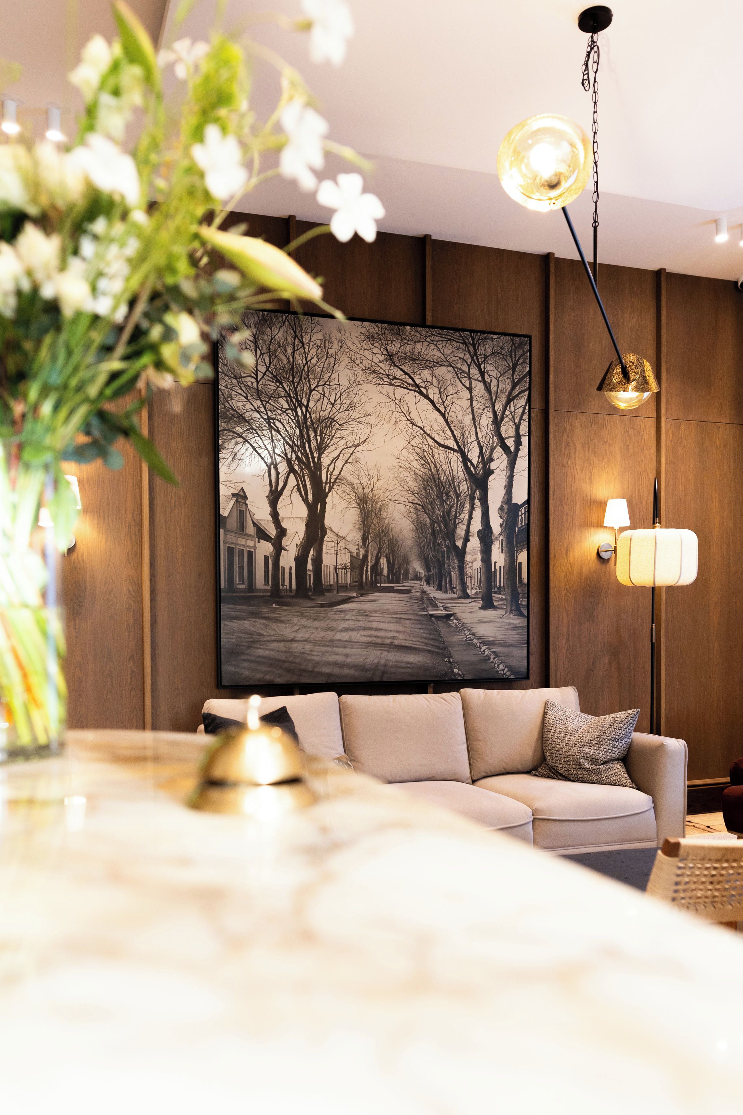 A living room with a sofa, a wall-mounted picture, a floor lamp, and a vase with flowers.