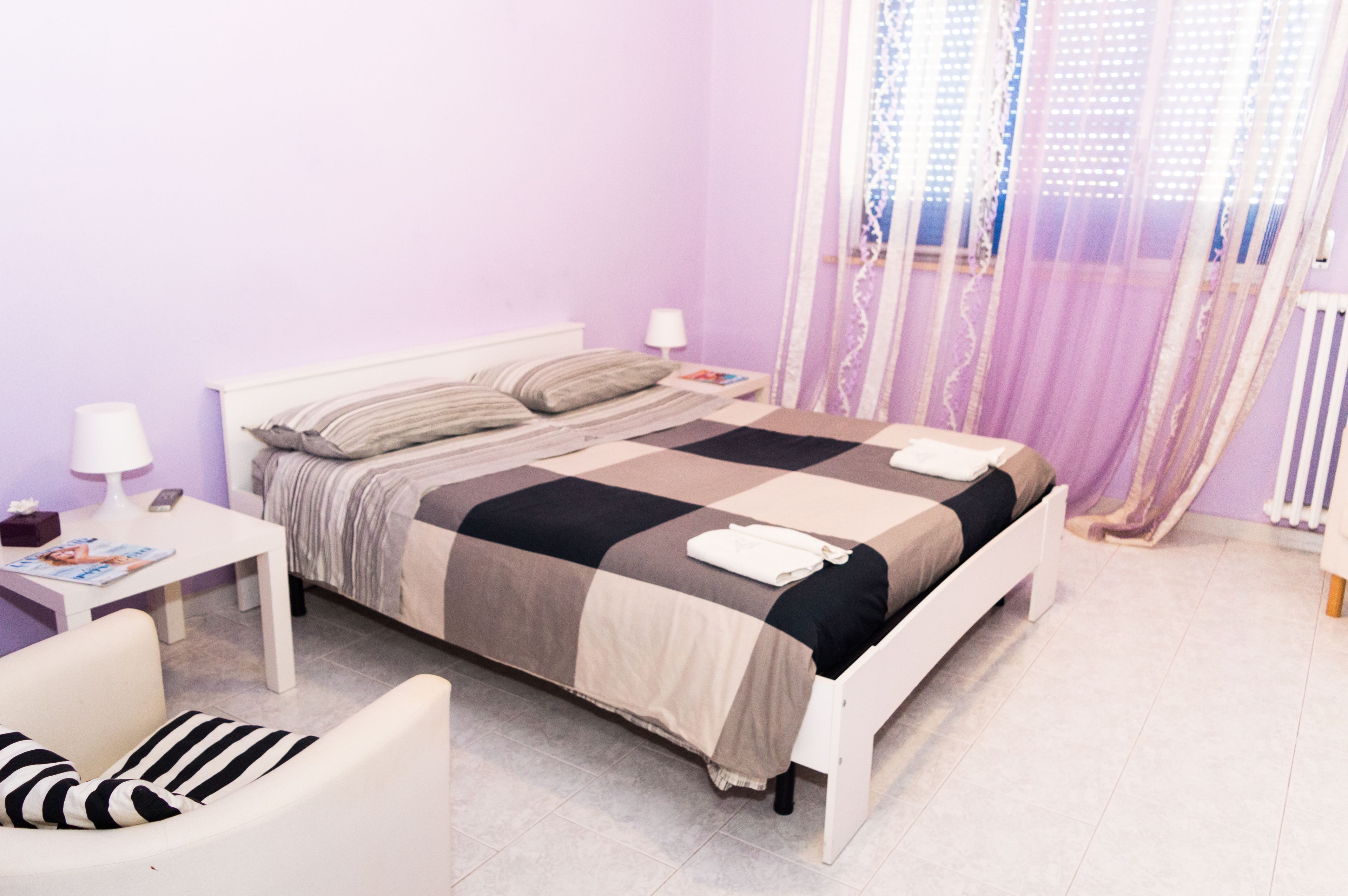 A neatly arranged bedroom with a bed, bedside tables, a chair, and a window with curtains.